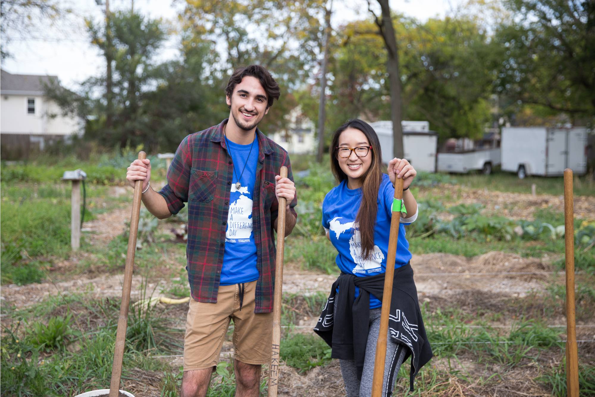 Two students smiling while holding shovels on a farm